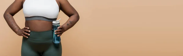 Cropped view of tattooed african american plus size woman holding sports bottle with water isolated on beige, banner — Stock Photo