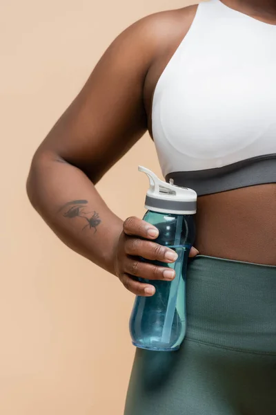 Cropped view of tattooed african american plus size woman holding sports bottle isolated on beige — Fotografia de Stock