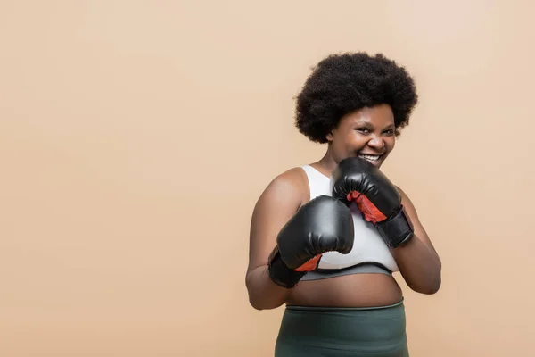 Cheerful african american plus size woman with boxing gloves isolated on beige — Stock Photo