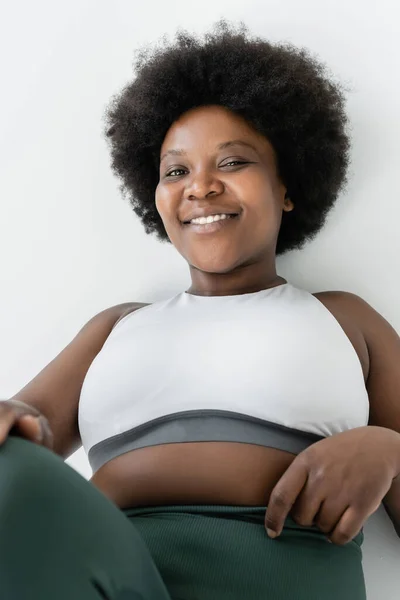 Joyful african american plus size woman in sportswear smiling isolated on white — Foto stock