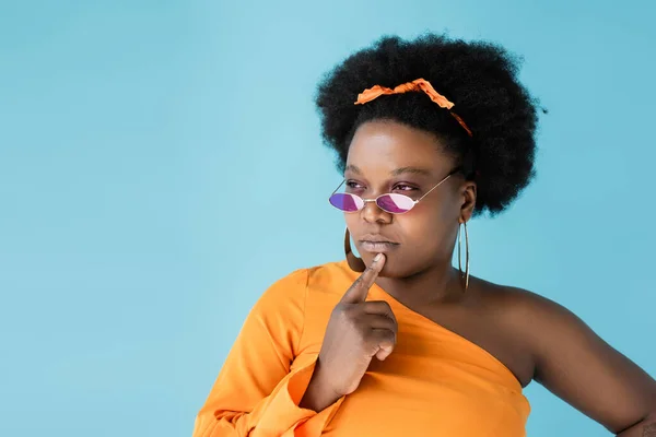 Pensive african american body positive woman in pink sunglasses isolated on blue — Stockfoto