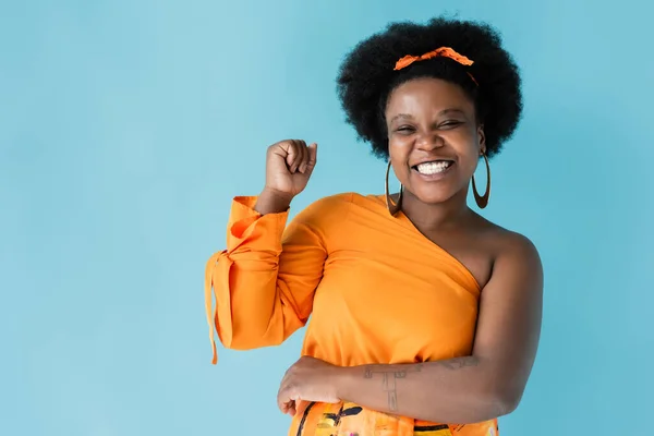Excited african american body positive woman in orange dress isolated on blue — Fotografia de Stock