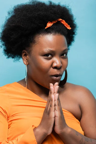 African american body positive woman with praying hands looking at camera isolated on blue — Fotografia de Stock