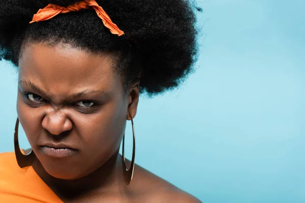 Portrait of angry african american body positive woman in hoop earrings looking at camera isolated on blue — Fotografia de Stock