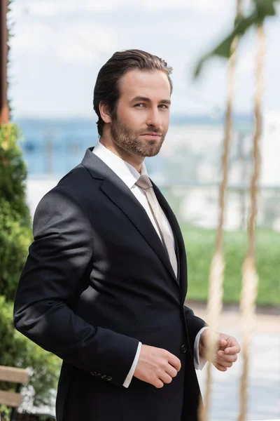 Elegant groom in black suit looking at camera on terrace — Fotografia de Stock