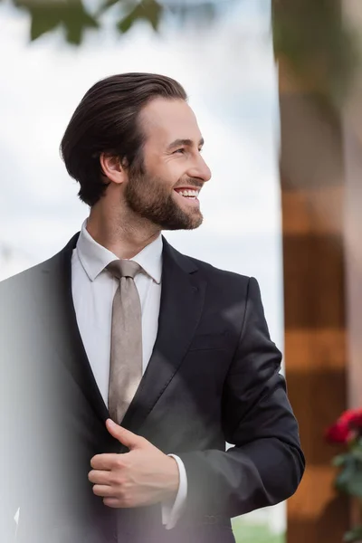 Side view of positive bearded groom in suit looking away outdoors — Stockfoto