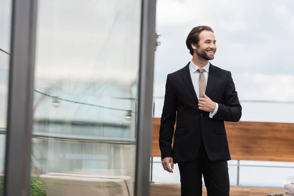 Young groom smiling while adjusting jacket on terrace — Stock Photo