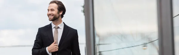 Positive groom adjusting jacket and looking away on terrace, banner — Stock Photo