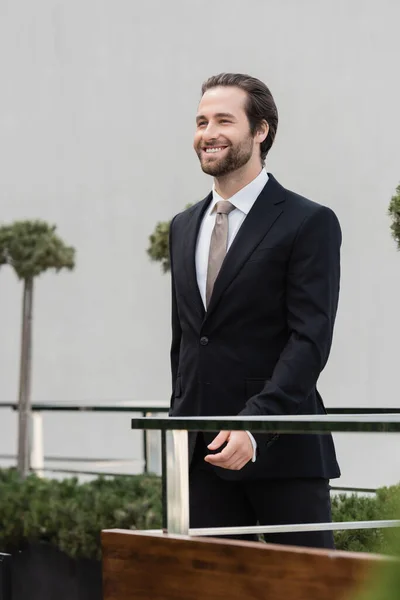 Cheerful groom in suit walking on terrace of restaurant — Stockfoto