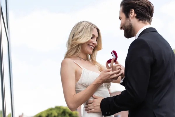 Низький кут зору усміхнений чоловік тримає заручини кільце біля дівчини в сукні на терасі — стокове фото