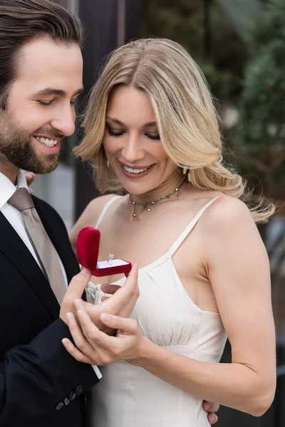 Smiling man in suit holding box with engagement ring near girlfriend outdoors — Stockfoto