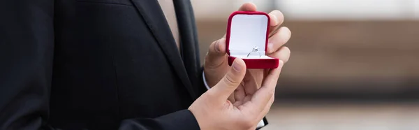 Cropped view of man in jacket holding box with engagement ring outdoors, banner — Stock Photo