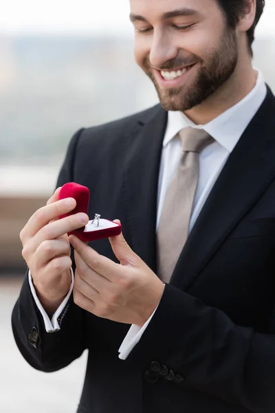 Smiling groom in suit holding box with ring outdoors — Stockfoto