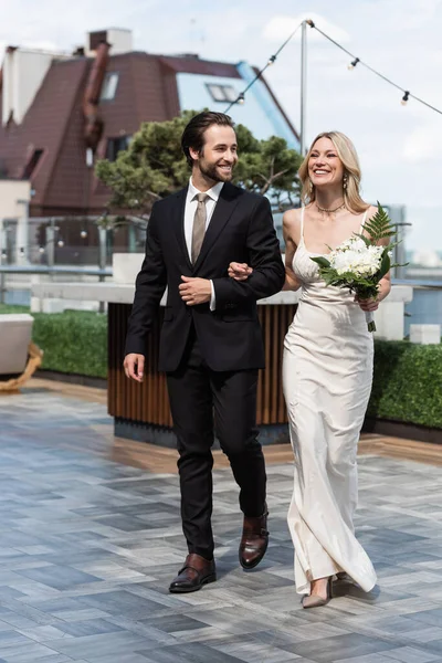 Allegro sposo in giacca e cravatta guardando la sposa bionda con bouquet sulla terrazza del ristorante — Foto stock