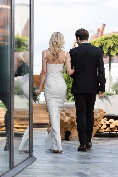 Back view of newlyweds with bouquet walking on terrace of restaurant — Fotografia de Stock