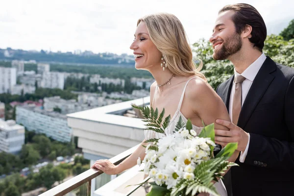 Side view of groom and wife with bouquet looking away from terrace — Stockfoto