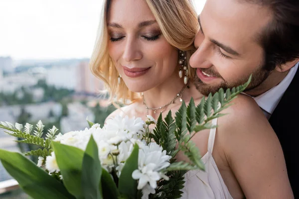 Smiling groom standing near bride with blurred bouquet on terrace — Foto stock