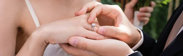 Cropped view of groom wearing ring on finger of bride outdoors, banner — Foto stock