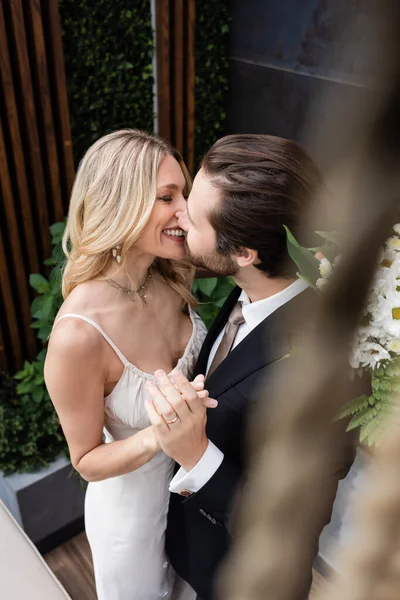 Smiling newlyweds with bouquet kissing on terrace of restaurant — Stock Photo