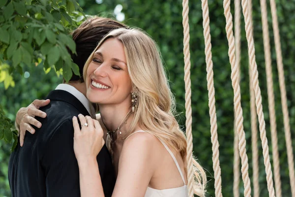 Happy bride in dress embracing groom outdoors — Stock Photo