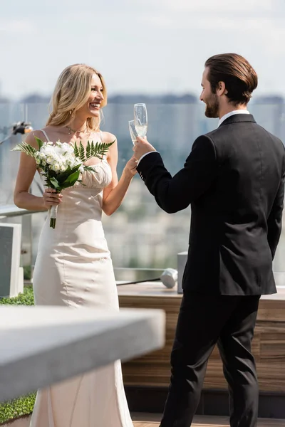 Cheerful newlyweds clinking with champagne on terrace of restaurant — Stockfoto