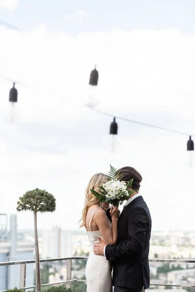 Sposi che coprono i volti con bouquet mentre si baciano sulla terrazza — Foto stock