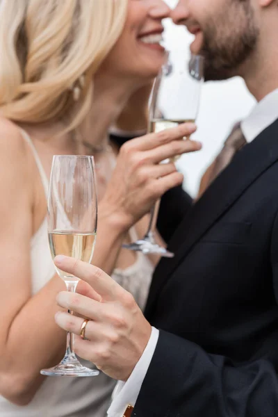 Cropped view of champagne in hand of groom kissing bride outdoors — Stock Photo