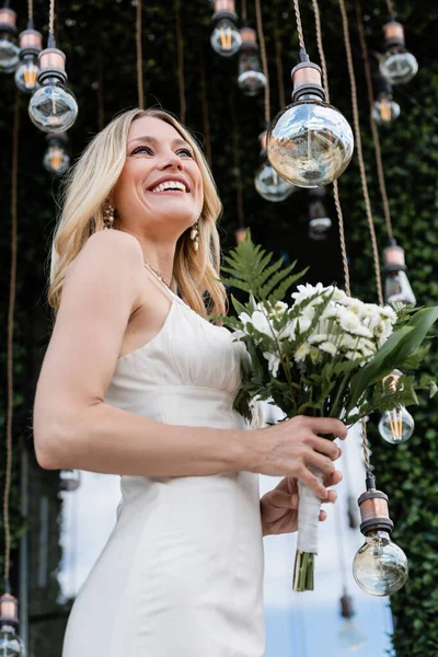 Low angle view of happy bride holding bouquet near light bulb on terrace — Foto stock