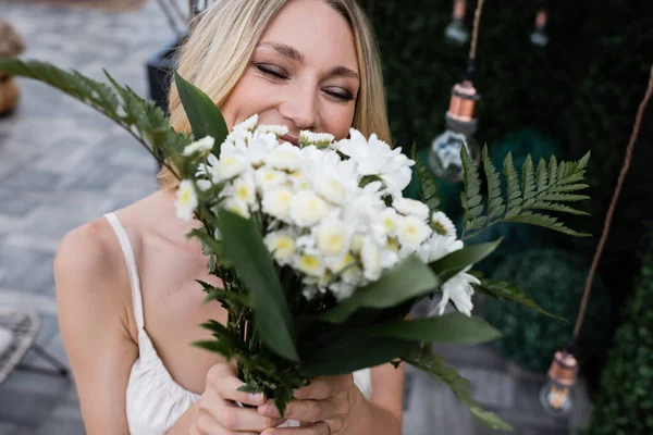 Blonde bride covering face with blurred bouquet on terrace — Stockfoto