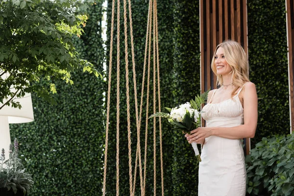 Positive bride holding flowers near plants on terrace — Photo de stock