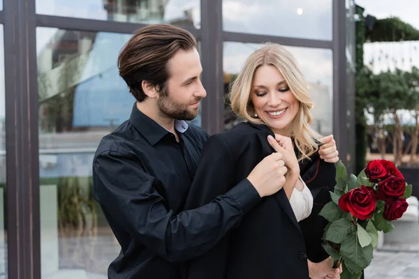 Молодой человек в куртке на улыбающейся девушке с розами на террасе — стоковое фото