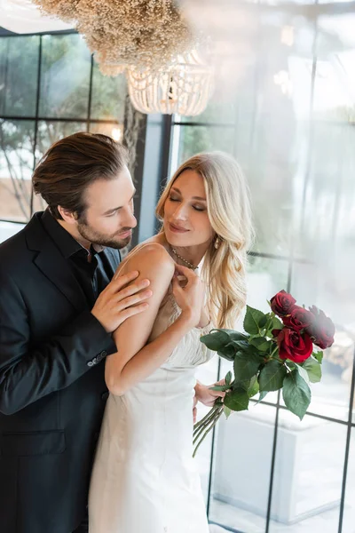 Young man touching blonde girlfriend with red roses in restaurant — Photo de stock