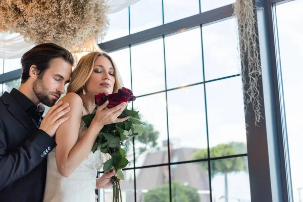 Young man touching shoulder of girlfriend with roses in restaurant — Stock Photo