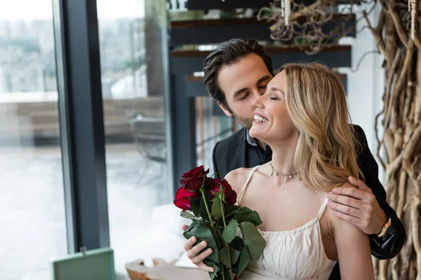 Чоловік Брюнета цілує веселу дівчину з червоними трояндами в ресторані. — стокове фото