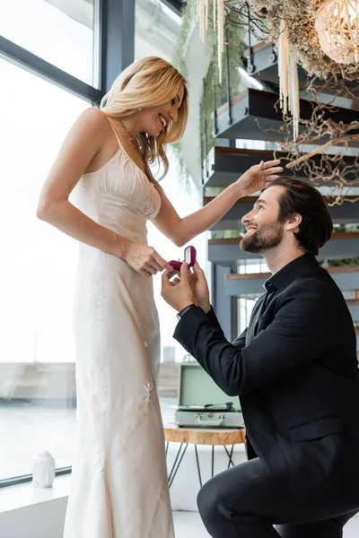 Vista laterale dell'uomo che tiene la scatola con anello di fidanzamento vicino alla ragazza allegra nel ristorante — Foto stock