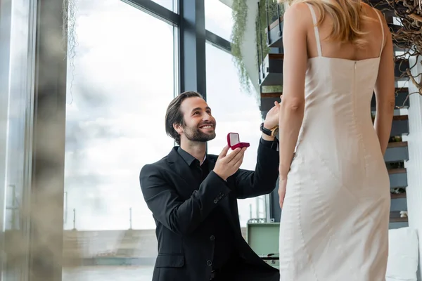 Smiling man holding box with engagement ring near girlfriend in dress in restaurant — Foto stock