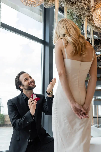 Позитивный мужчина держит обручальное кольцо рядом с девушкой в платье в ресторане — стоковое фото