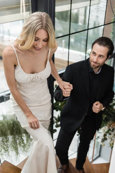 Smiling woman in dress holding hand of blurred boyfriend on stairs in restaurant — Stockfoto