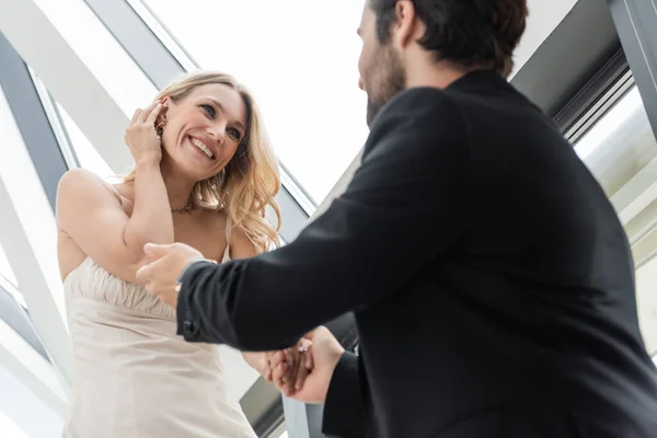 Low angle view of blurred man holding hand of cheerful girlfriend in dress in restaurant — Foto stock