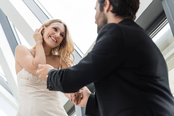 Low angle view of blurred man holding hand of cheerful girlfriend in dress in restaurant — Fotografia de Stock