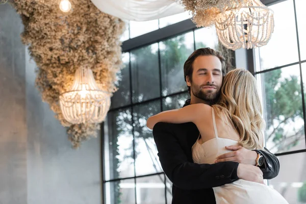 Bearded man in suit hugging blonde girlfriend in restaurant — Stock Photo