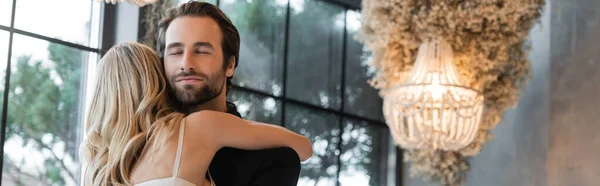 Blonde woman embracing elegant boyfriend with closed eyes in restaurant, banner — Photo de stock