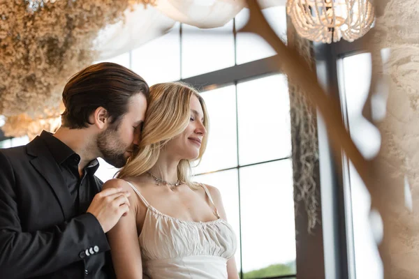 Young man in suit touching shoulder and smelling hair of blonde girlfriend in restaurant — Fotografia de Stock