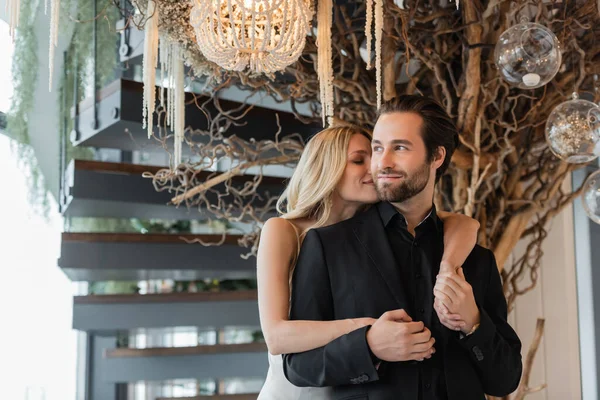 Blonde woman kissing and holding hands of elegant boyfriend in restaurant — Stock Photo