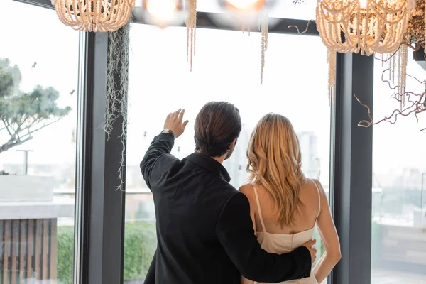 Back view of man in suit hugging girlfriend and pointing with hand in restaurant — Stock Photo