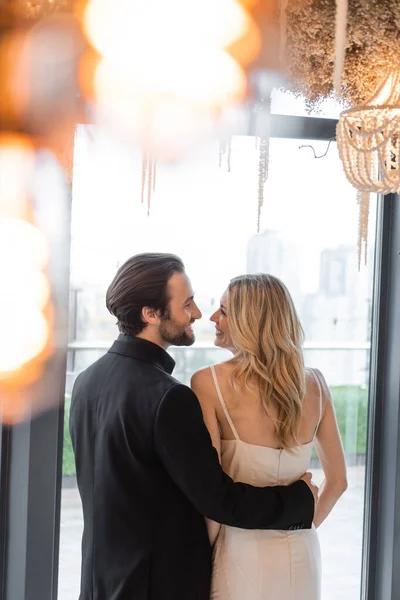 Side view of smiling man in suit hugging blonde girlfriend in restaurant — Stock Photo