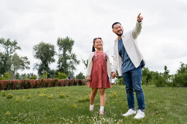 Cheerful asian daughter and dad looking away in summer park — Photo de stock
