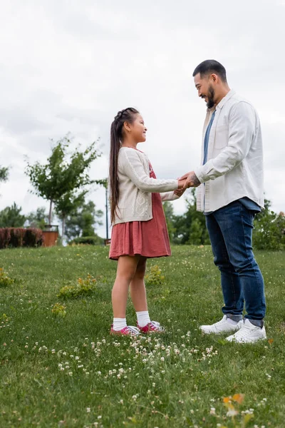 Вид сбоку улыбающегося отца и ребенка, держащихся за руки в летнем парке — стоковое фото