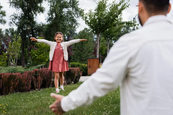 Cheerful asian kid walking on grass near blurred dad in park — Foto stock