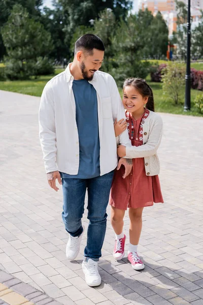 Cheerful father and asian daughter walking in park — Fotografia de Stock